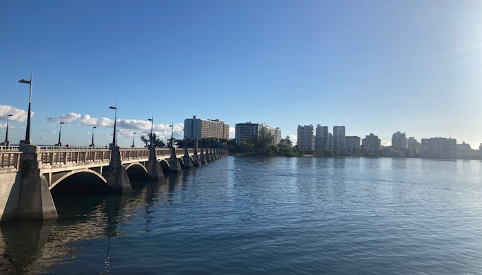 a bridge over water with buildings in the background in Condado lagoon