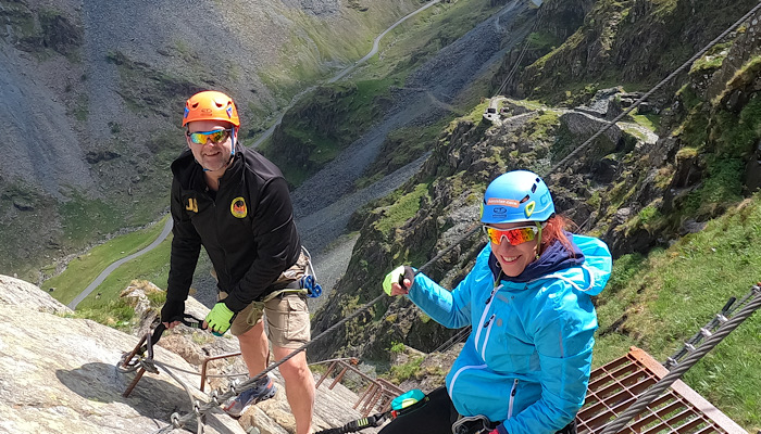 a man and woman wearing helmets and climbing on a rock wall