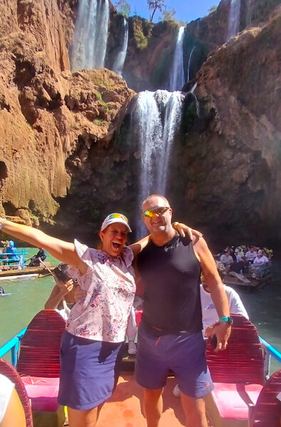 a man and woman standing in a boat with a waterfall behind them